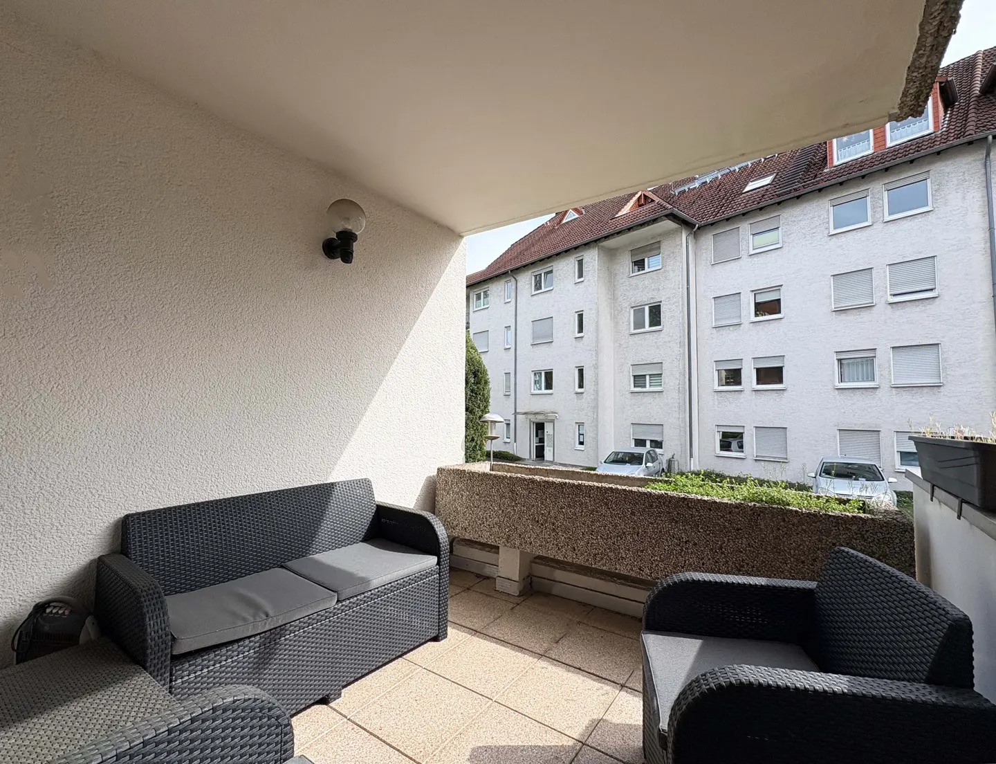 A balcony with black wicker furniture, including a sofa and chair, overlooks a white apartment building.