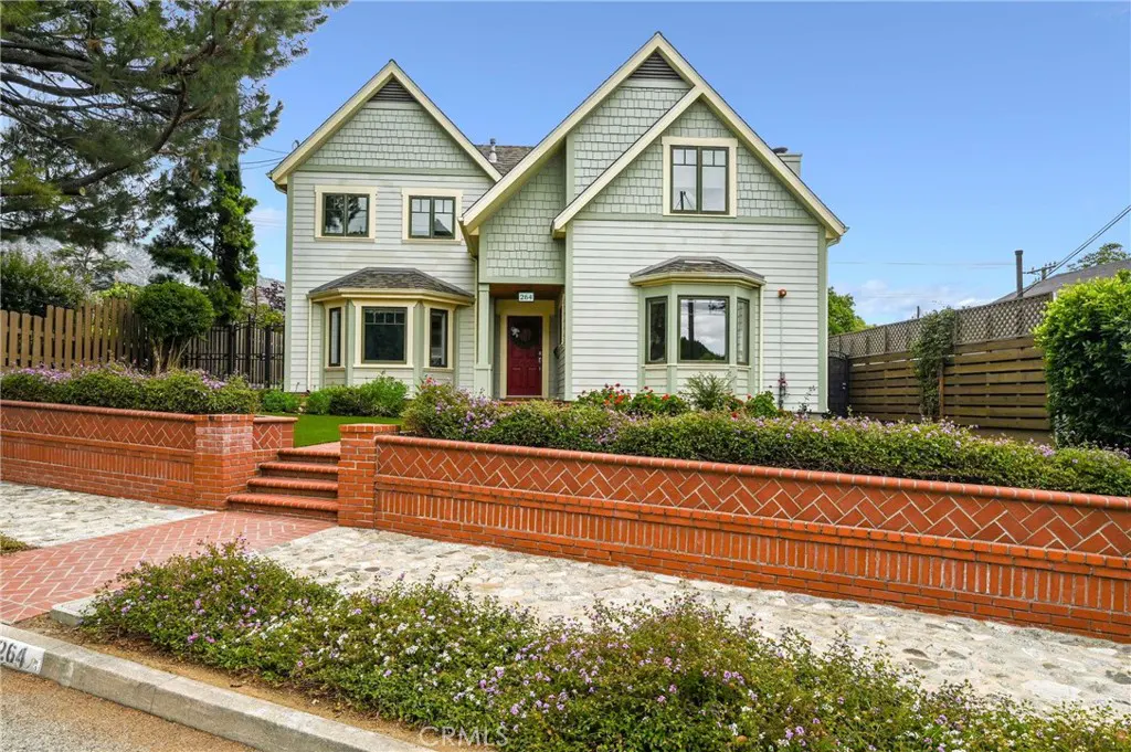 Two-story house with light green siding and a red door. A brick wall with flowers lines the front yard.