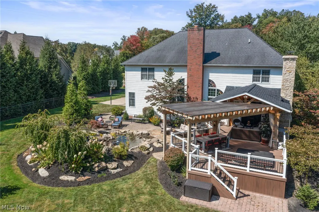 Aerial view of a white house with a large deck, pergola, pond, and patio furniture in the backyard.