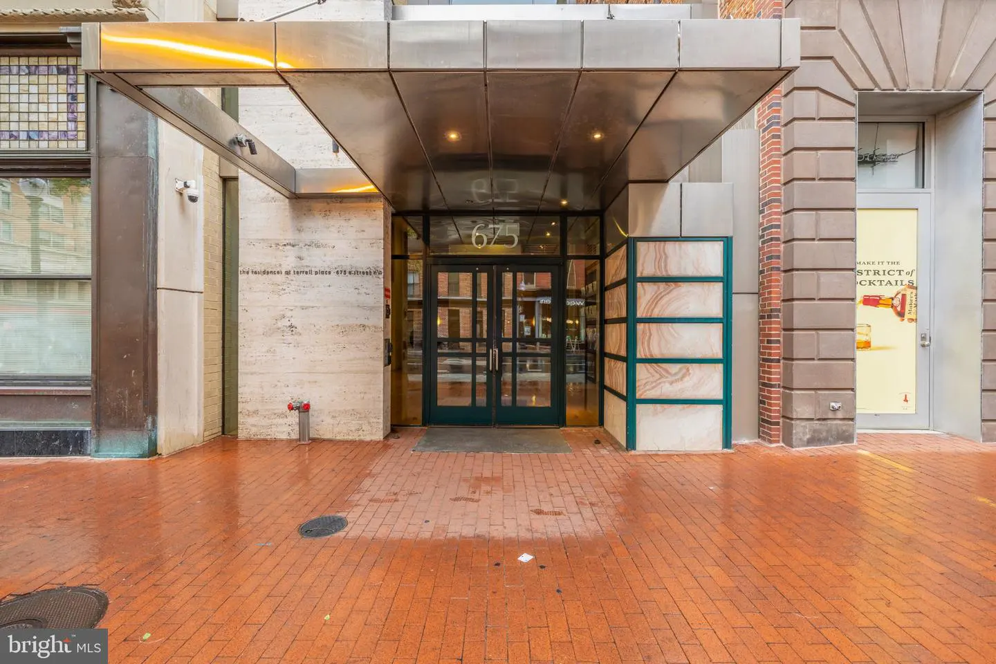 Building entrance with a metal awning and glass doors. The address "675" is above the doors. The sidewalk is brick.