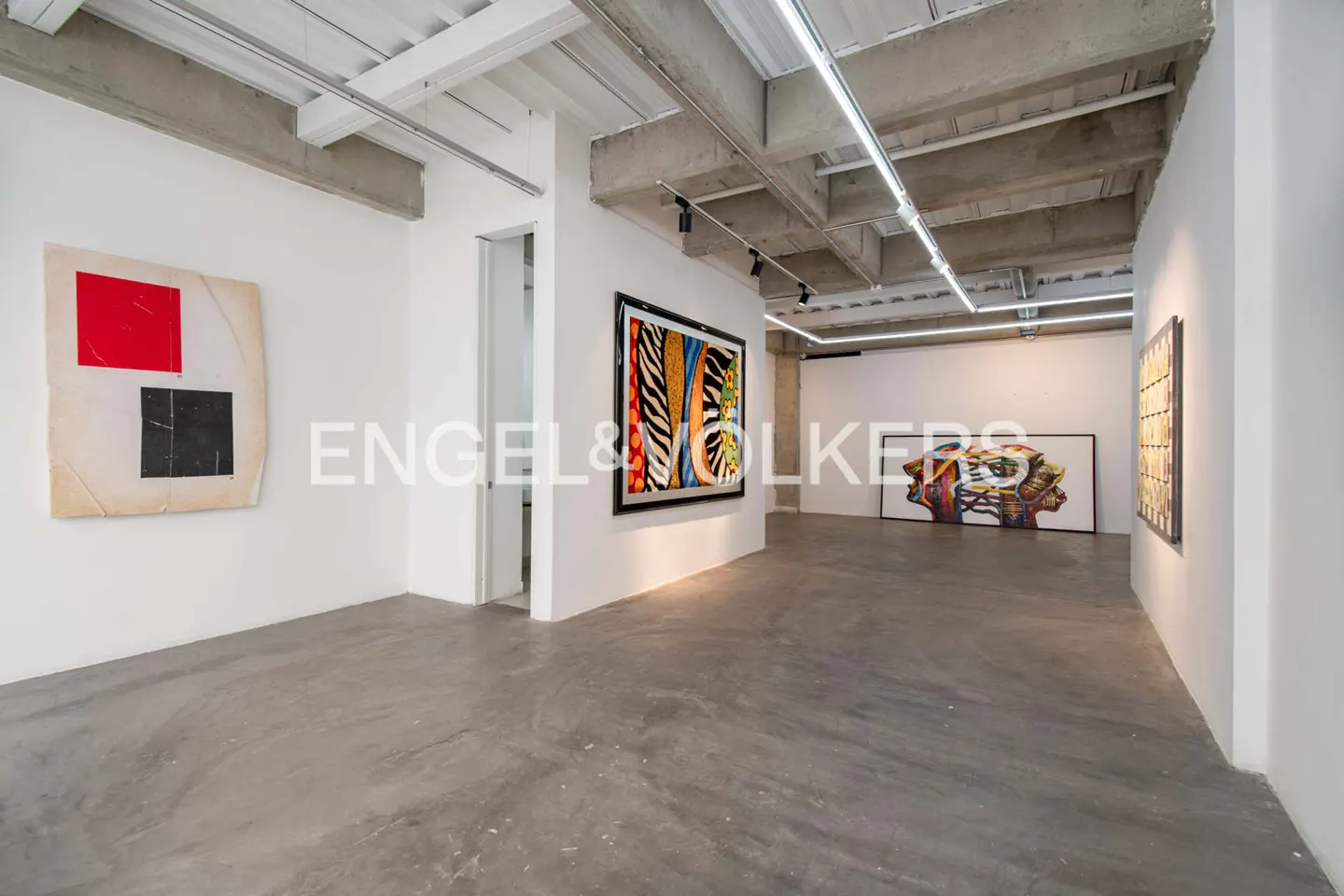 Gallery space with white walls, concrete floors and ceiling, and modern art pieces.