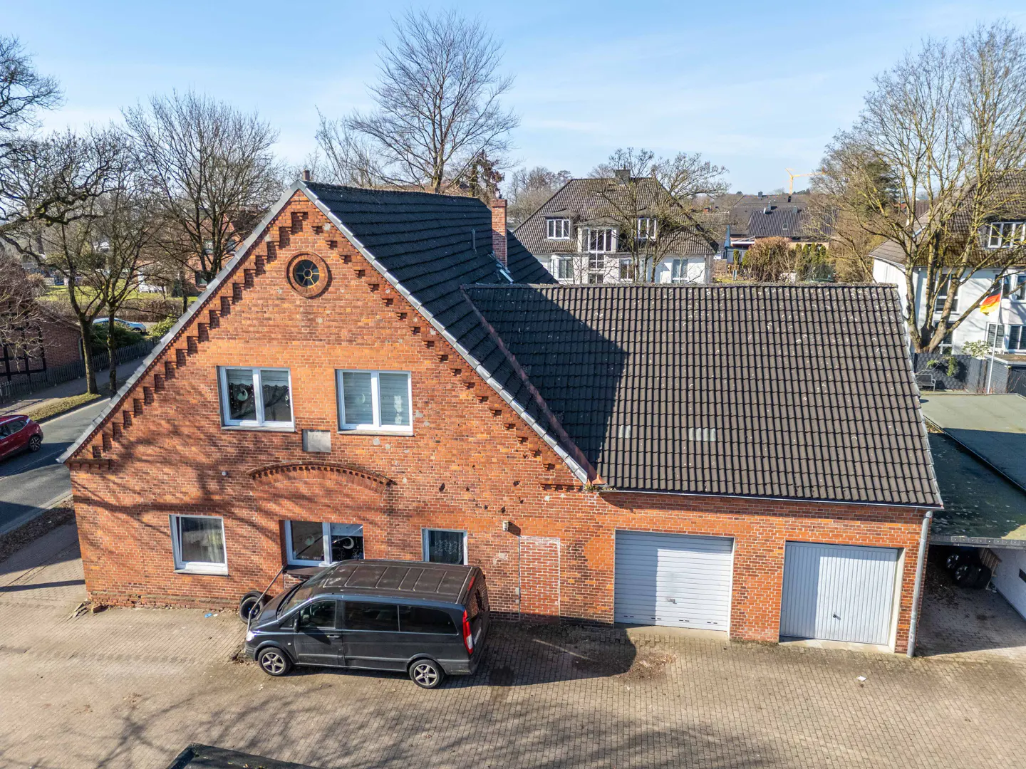 Aerial view of a two-story brick house with a dark gray roof and two garage doors, a black van parked in front.