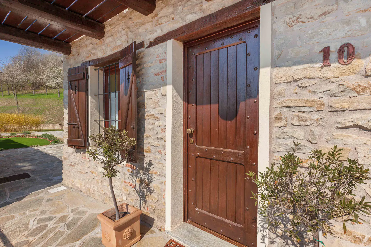 Exterior view of a stone house with a dark wood door, shutters, and the number 10 on the wall.