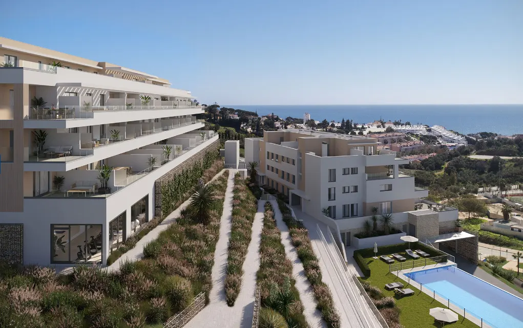 Modern apartment complex with balconies overlooking the ocean, pool, and landscaped grounds under a clear blue sky.