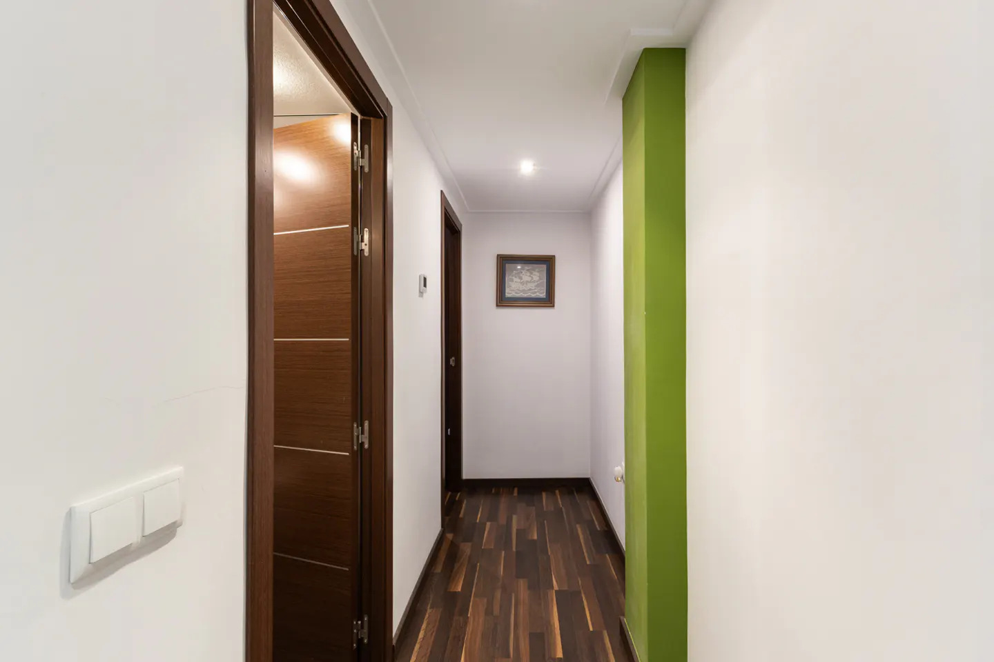 Hallway with dark wood floors, white walls, and a green accent wall. A partially open wood door is on the left.