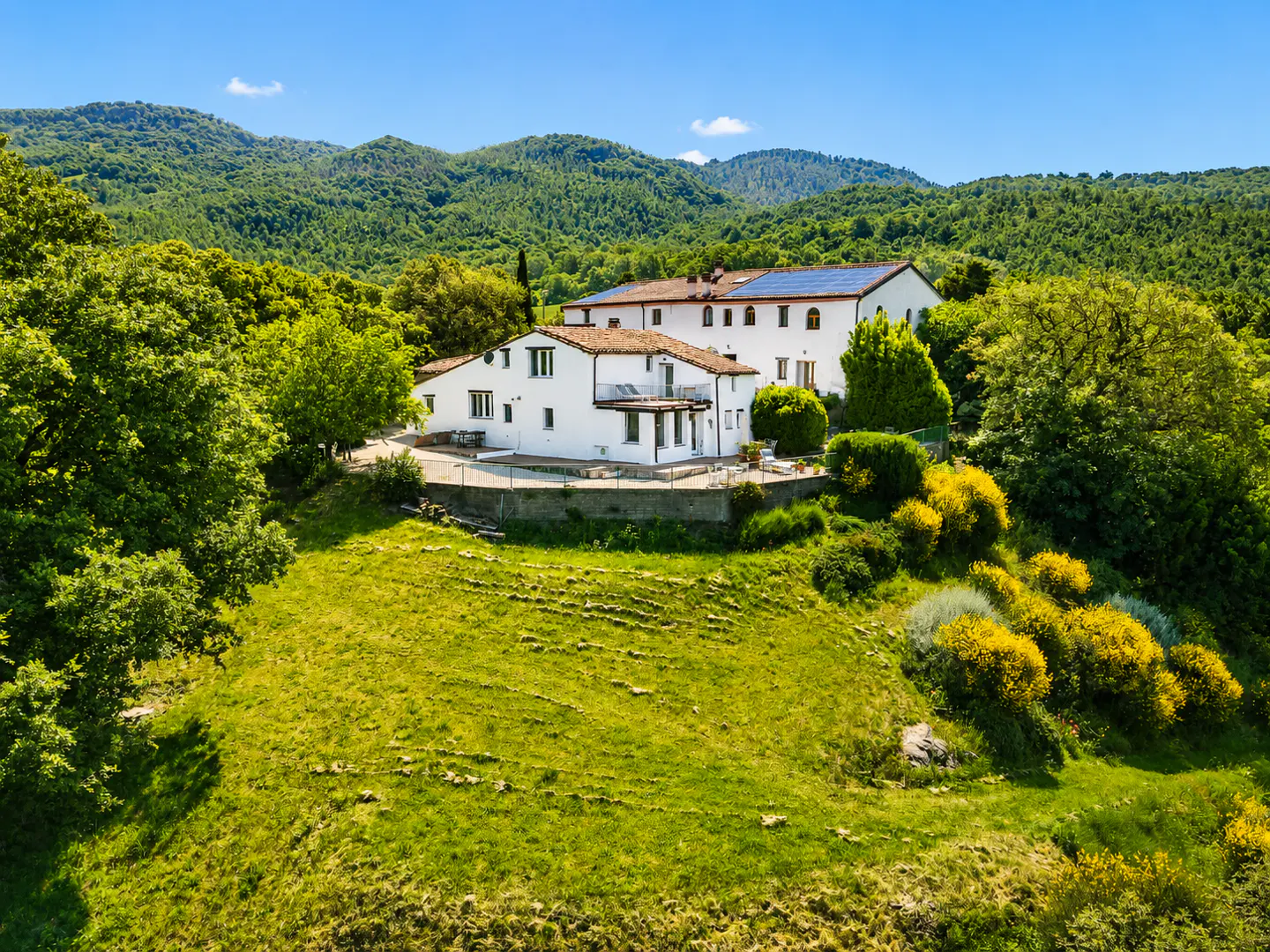 White villa with solar panels nestled in a lush green hillside landscape under a clear blue sky.