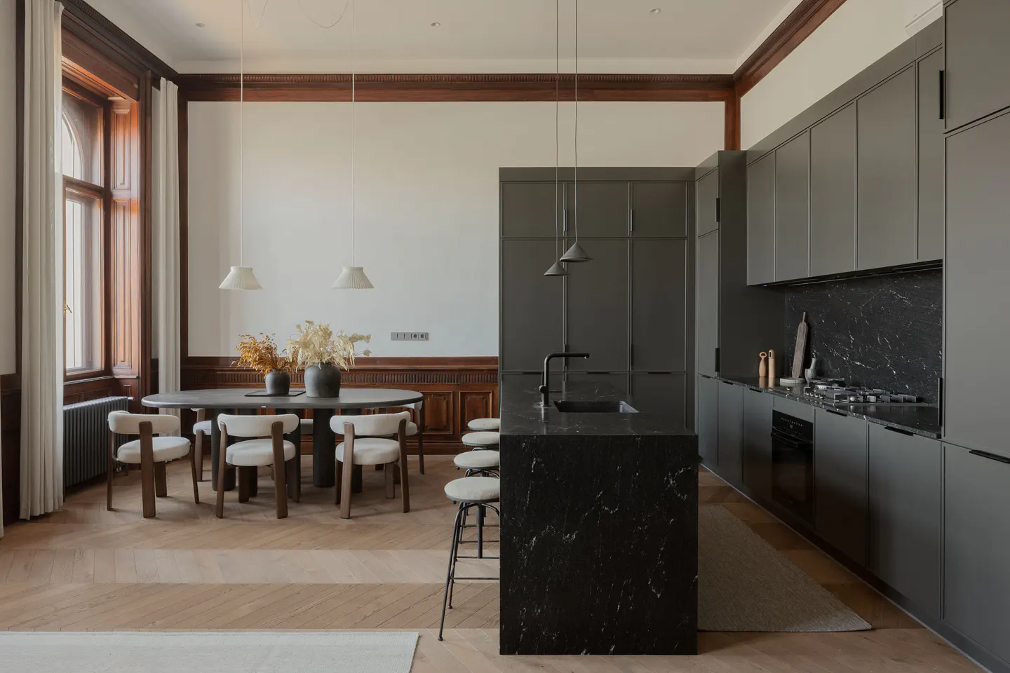 A modern kitchen and dining area with gray cabinets, a black marble island, and a round dining table with cream-colored chairs.