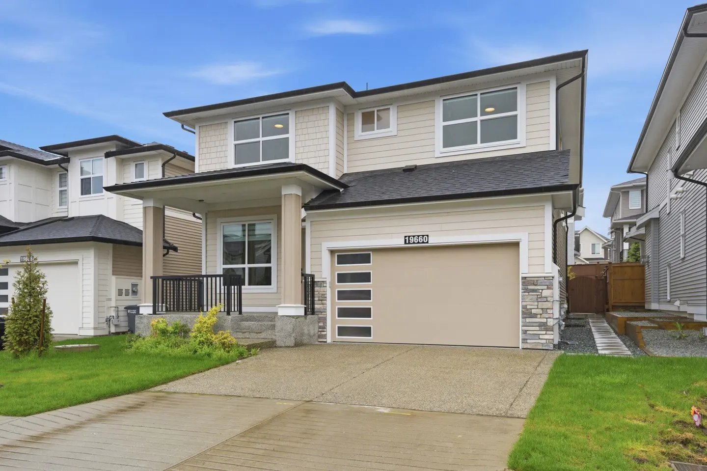 Two-story beige house with a front porch, a two-car garage, and a green lawn under a blue sky.