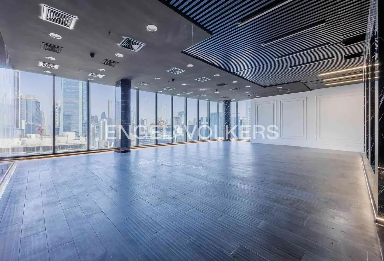 Empty office space with blue wood floors, floor-to-ceiling windows, and a city view. The ceiling is gray with recessed lighting and vents.