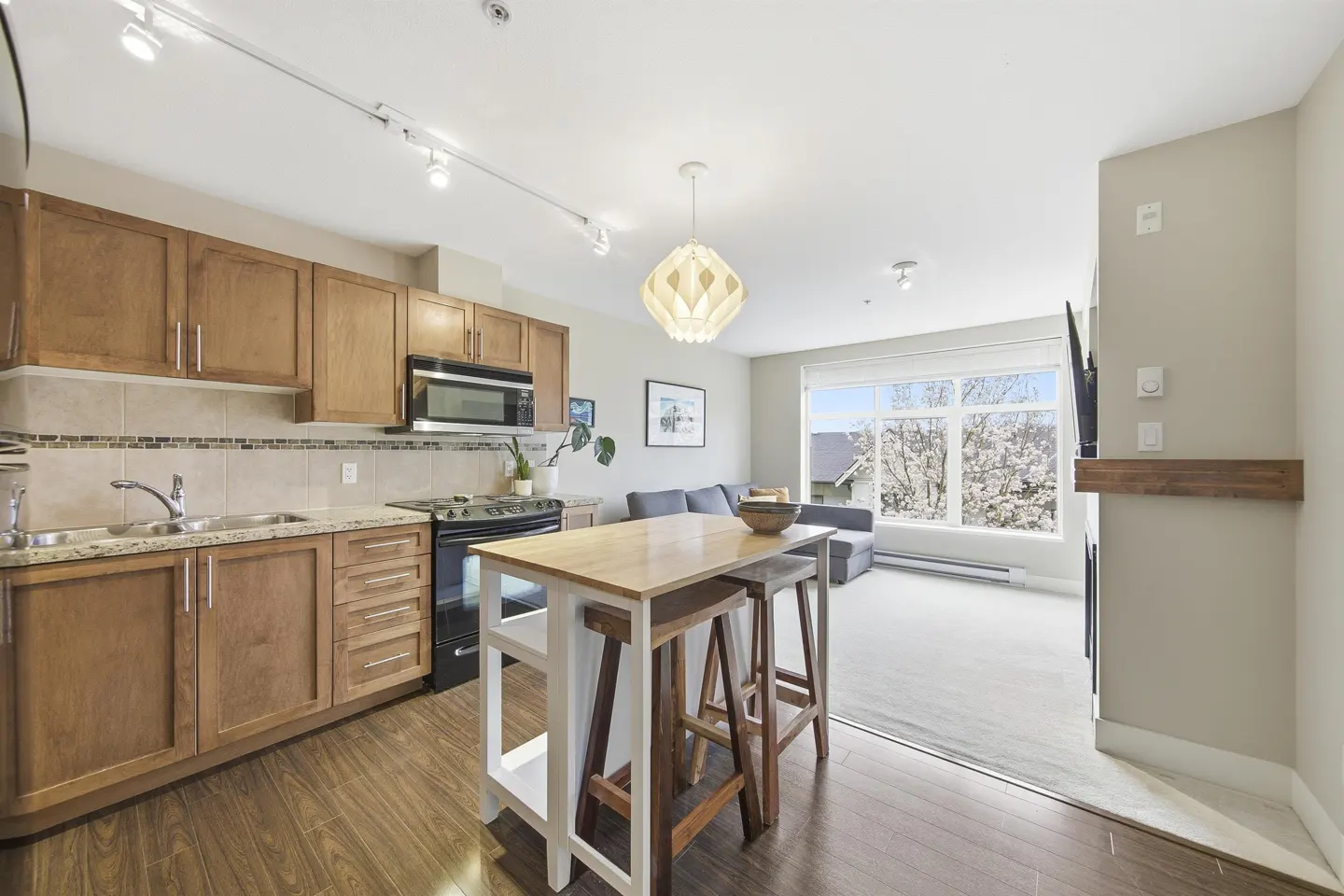 A bright, open-concept condo with wood floors, a kitchen island, and a view of blossoming trees.