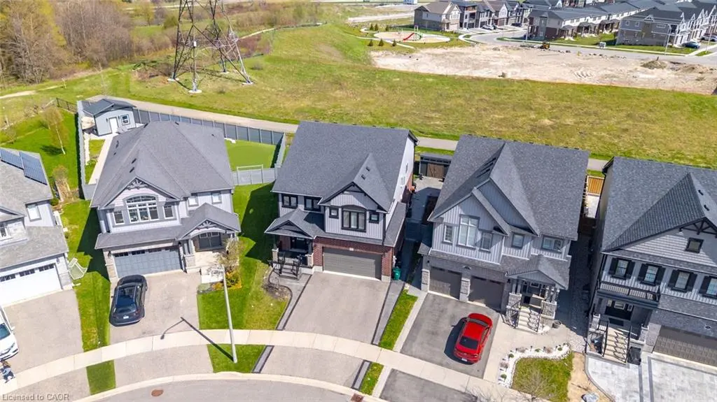Aerial view of three modern, two-story homes with gray siding and dark roofs, cars in driveways, and a green field in the background.