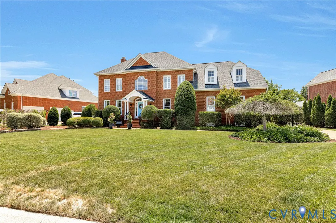 Brick two-story house with a blue door, white trim, and a large green lawn under a clear blue sky.