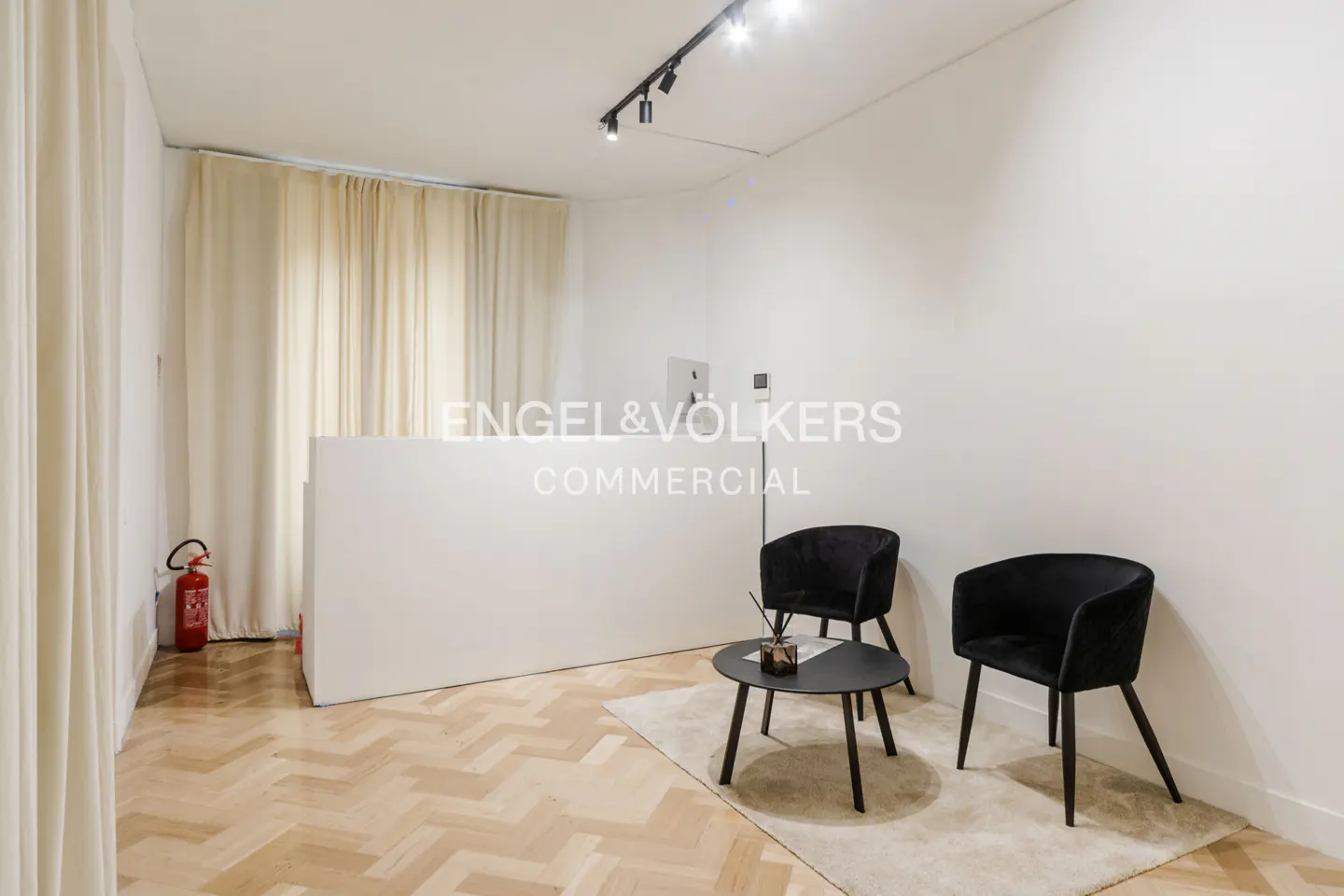 Bright office space with white walls, herringbone floors, and cream curtains. Black chairs and a table sit on a white rug.
