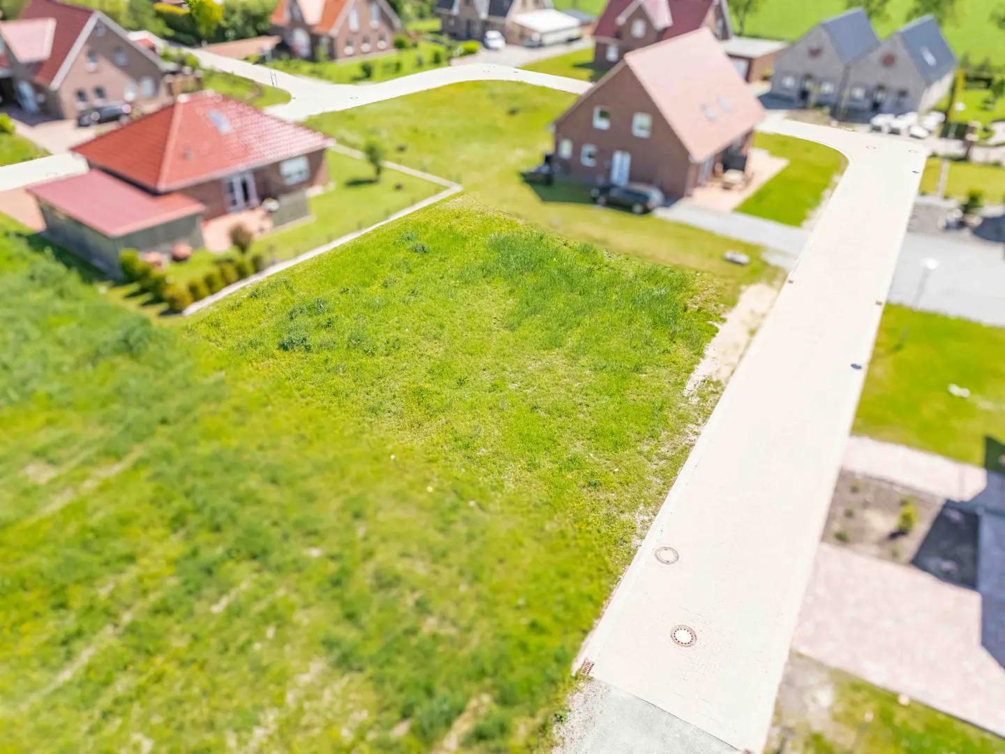 Aerial view of a grassy residential building plot with a concrete walkway in a suburban neighborhood of brick houses.