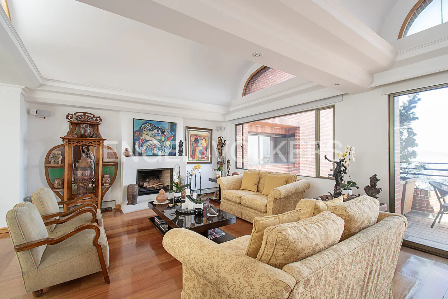 Bright living room with hardwood floors, two patterned sofas, fireplace, and large windows with a view.