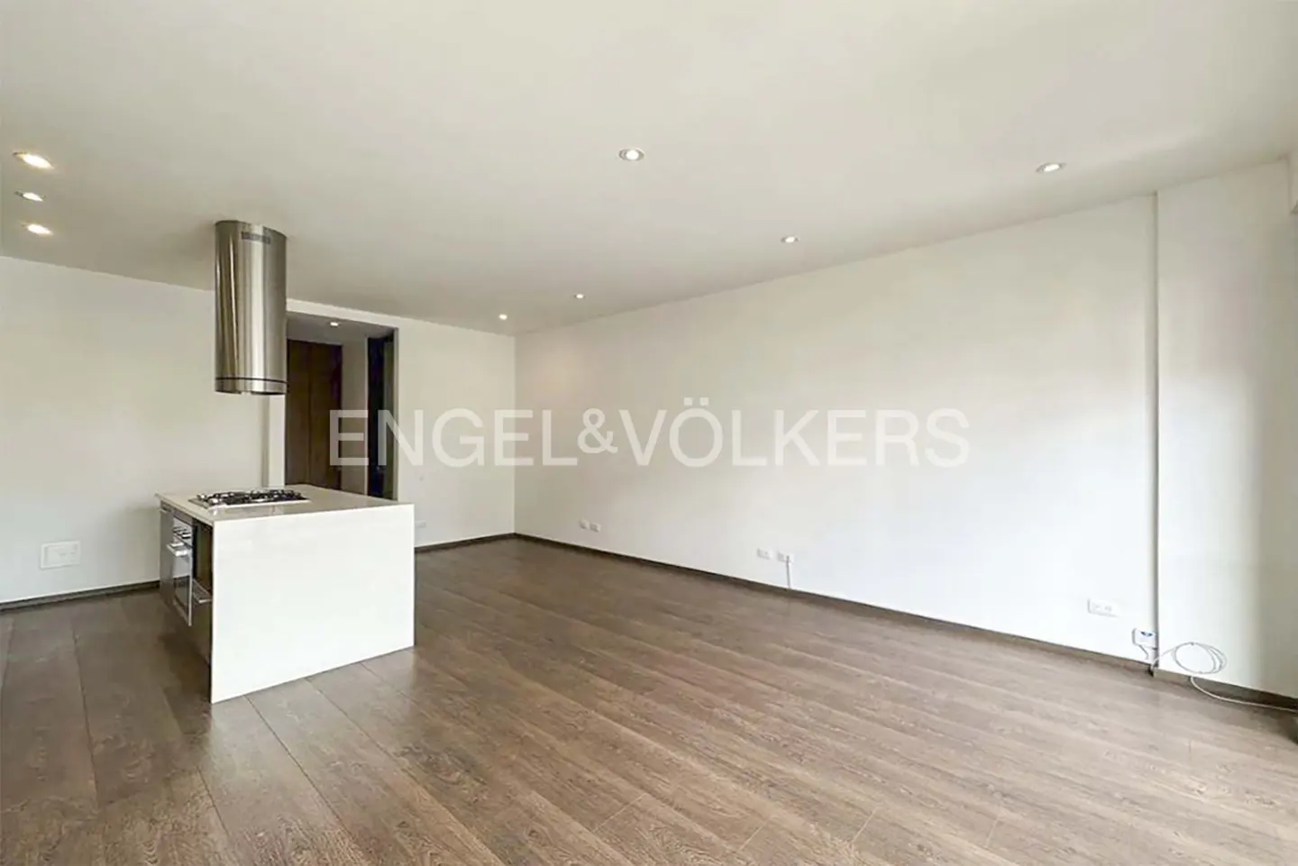 Bright, modern apartment with hardwood floors, white walls, and a kitchen island with a stainless steel range hood. Engel & Völkers logo visible.