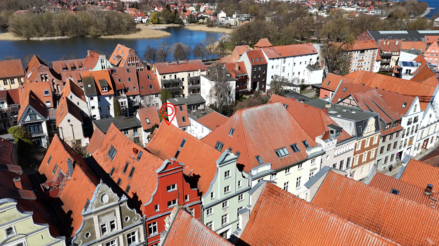 Aerial view of a European town with red-tiled roofs, a lake in the background, and a red location pin on a roof.