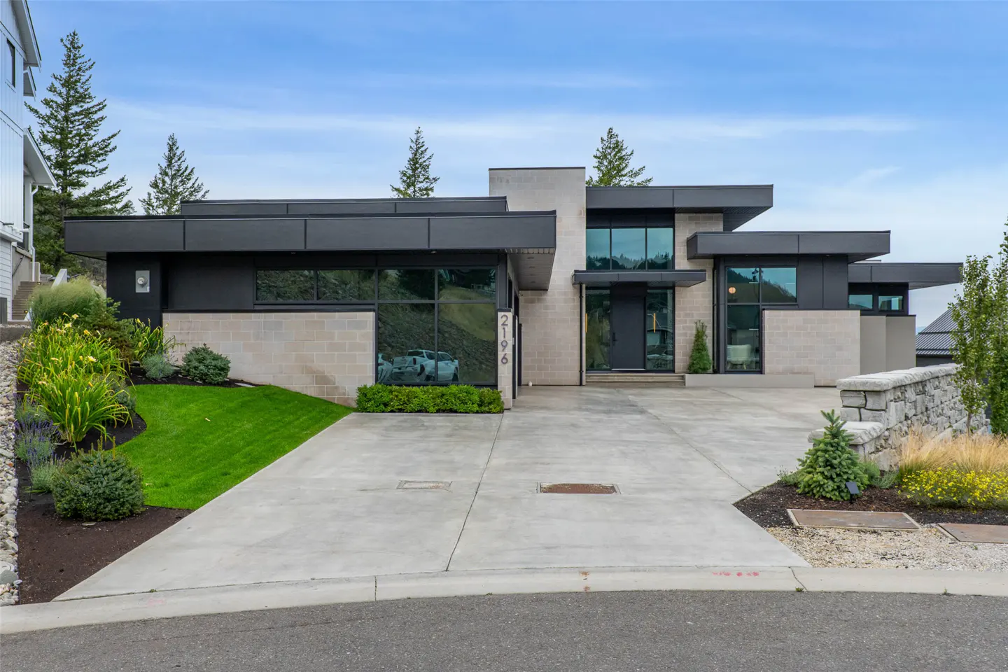 Modern single-story home with black metal accents, light stone walls, large windows, and a concrete driveway.