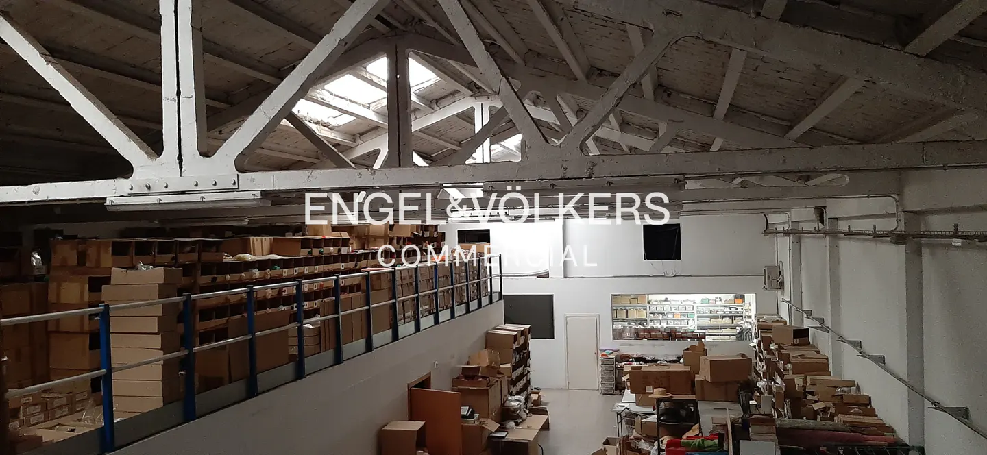 Interior view of a commercial warehouse with boxes, white walls, and a high ceiling with skylights. The Engel & Völkers logo is visible.