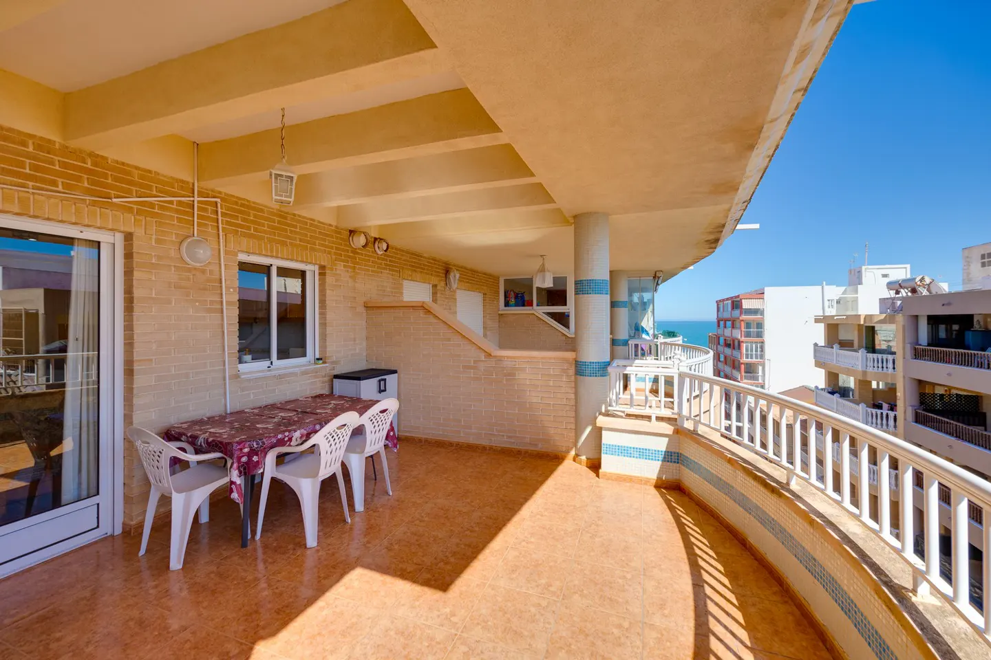 A sunny balcony with a table, chairs, and a view of the ocean and buildings.