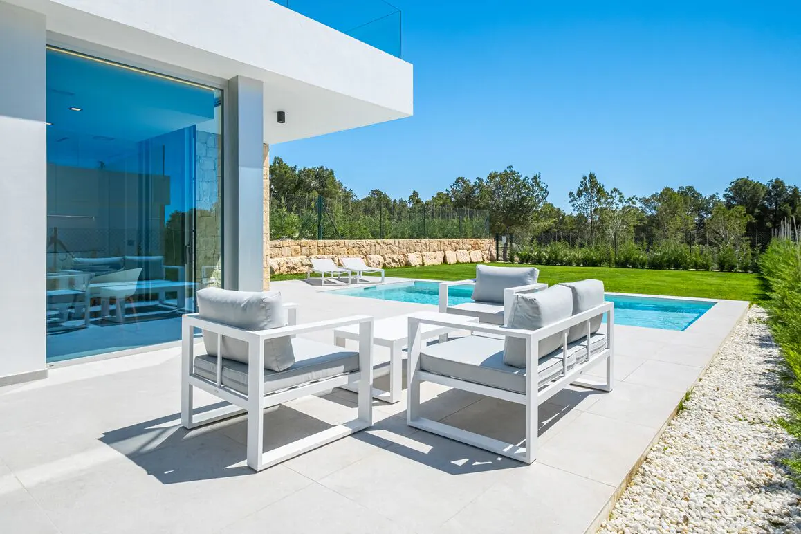 Modern white patio furniture with gray cushions sits beside a pool on a sunny day.