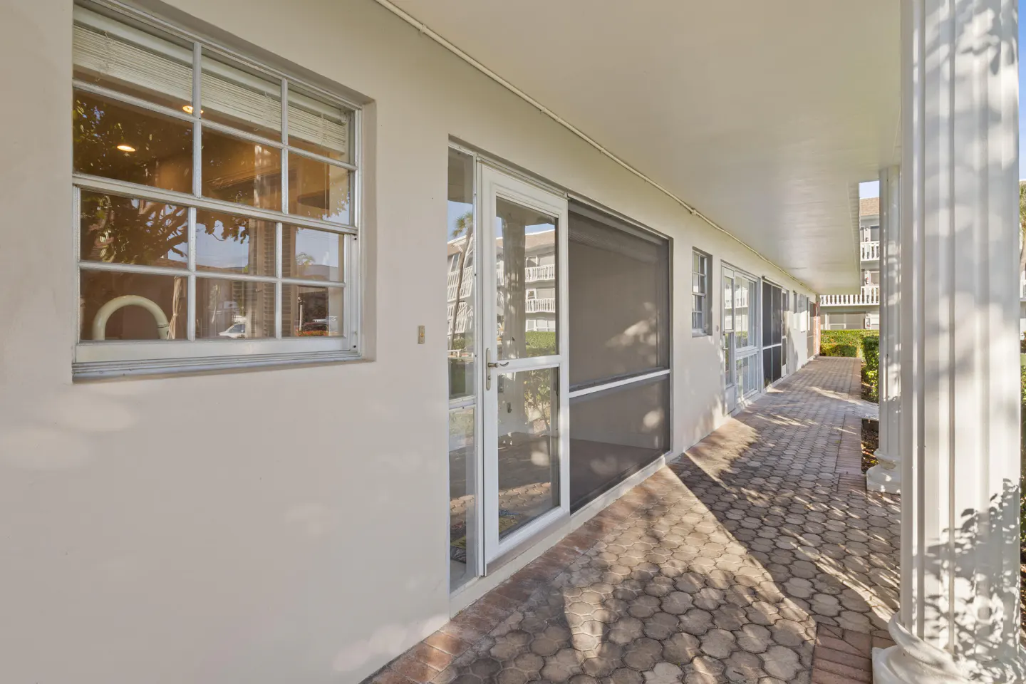 Exterior view of a white building with a brick walkway, windows, and screened doors under a covered walkway.
