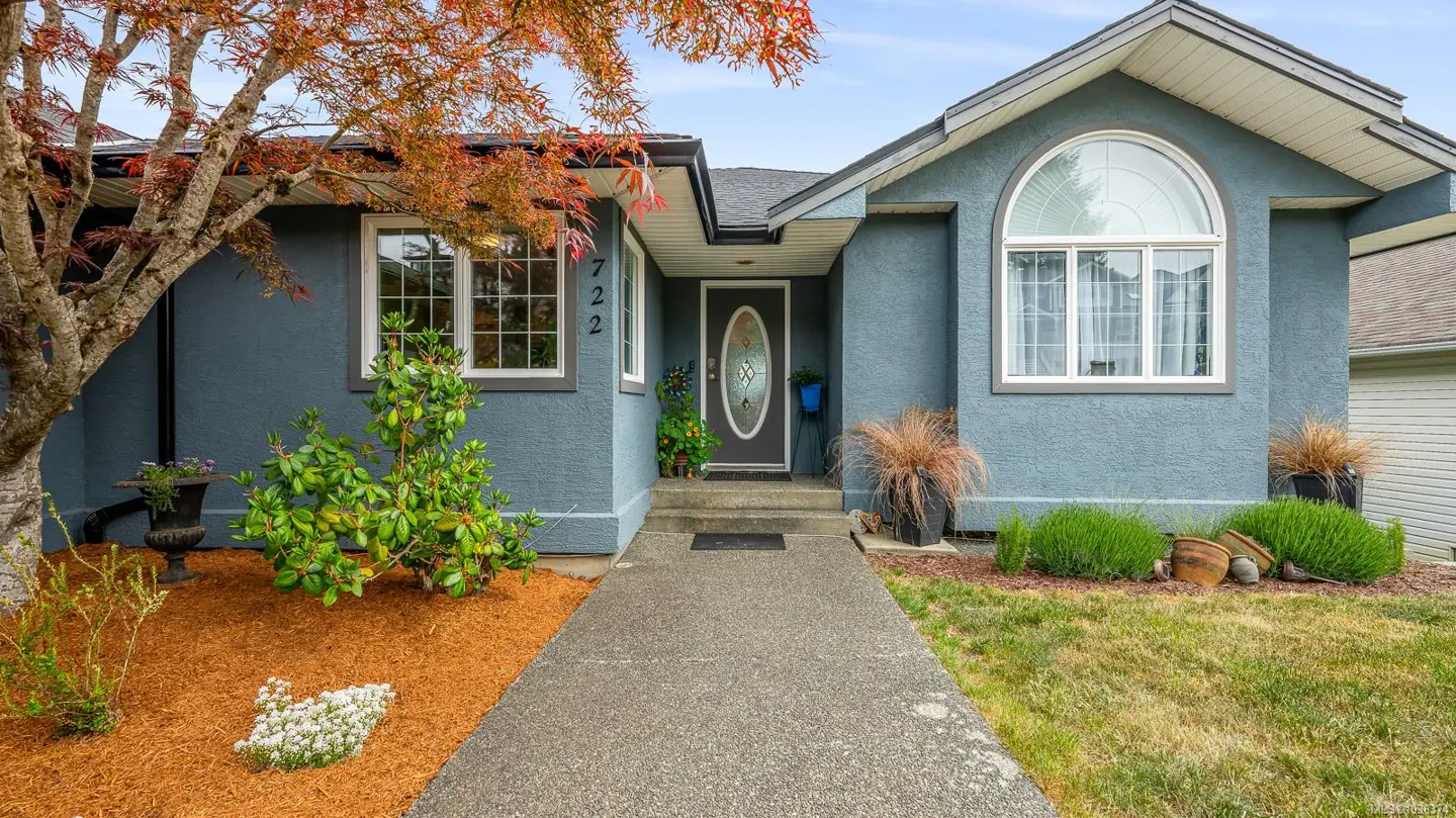 A blue single-story house with a gray door and white trim, surrounded by landscaping.