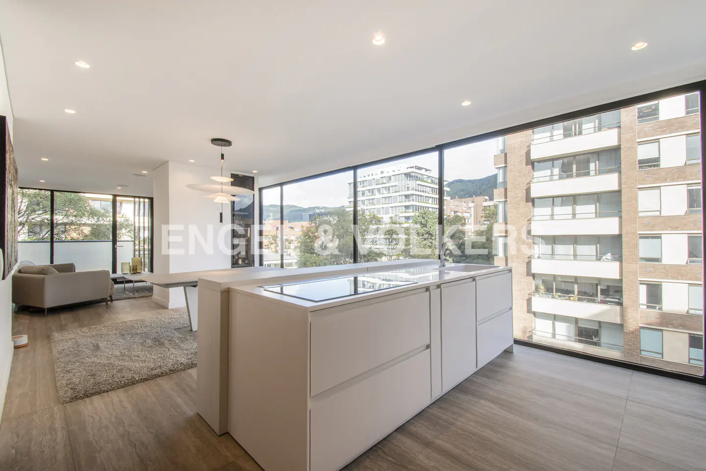 Bright, modern apartment interior with a white kitchen island, wood floors, and large windows overlooking a city view.