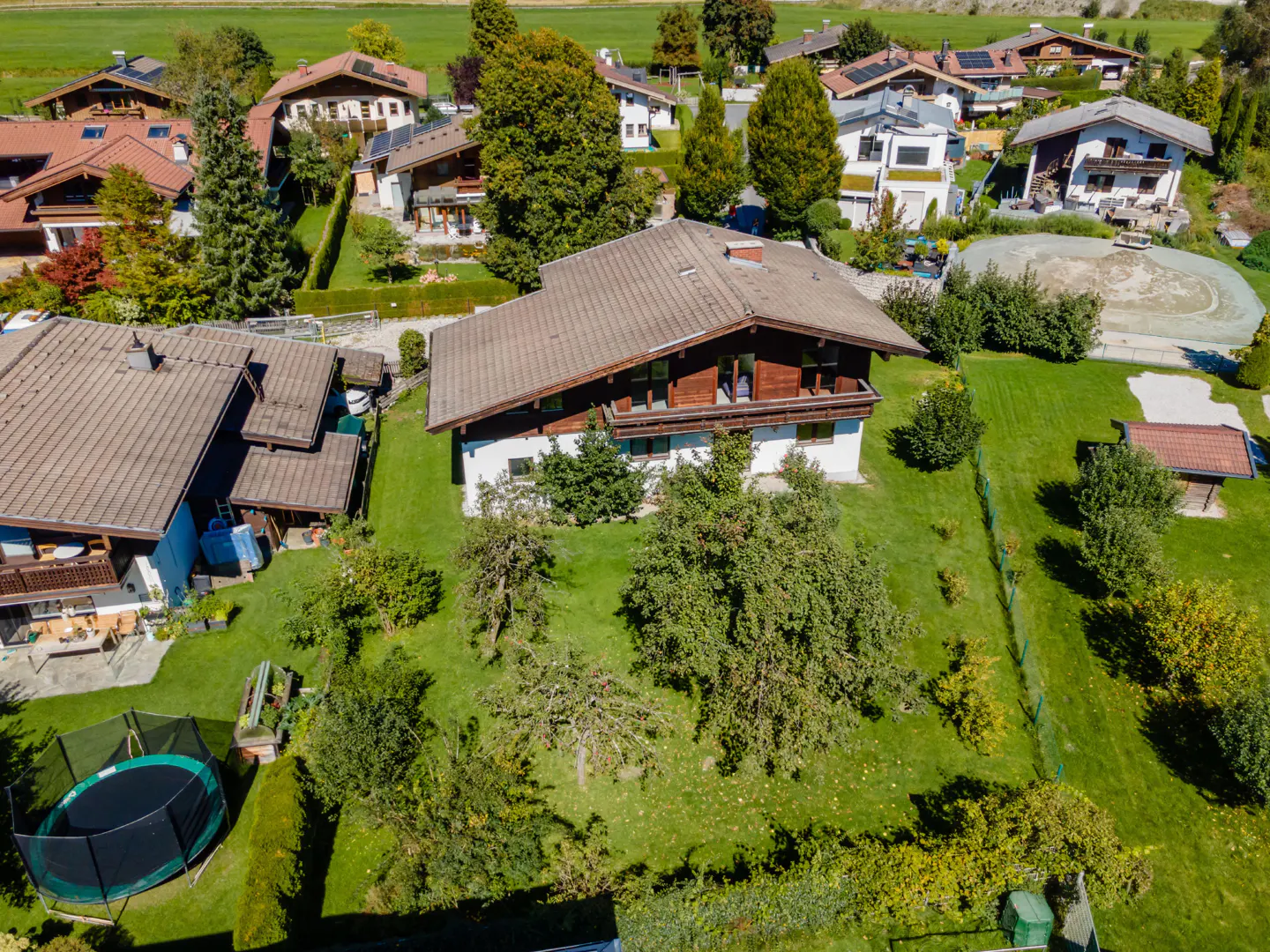 Aerial view of a two-story house with a brown roof and white walls, surrounded by green grass and trees.