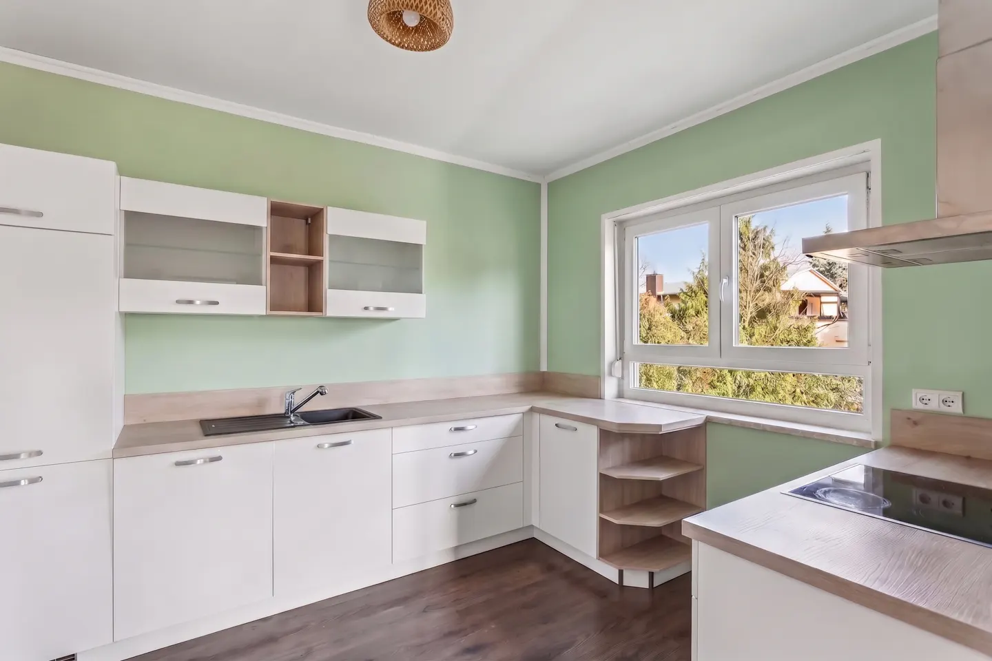 Kitchen with white cabinets, light wood countertops, sage green walls, and a window overlooking trees.