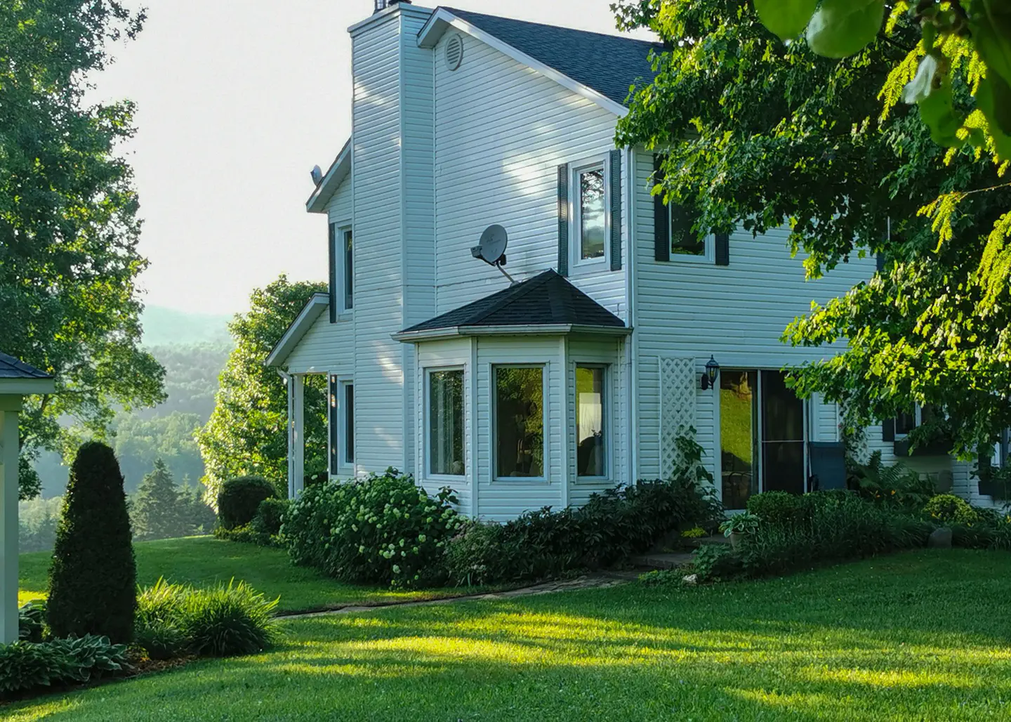 Exterior view of a two-story white house with a chimney, bay window, and green lawn.