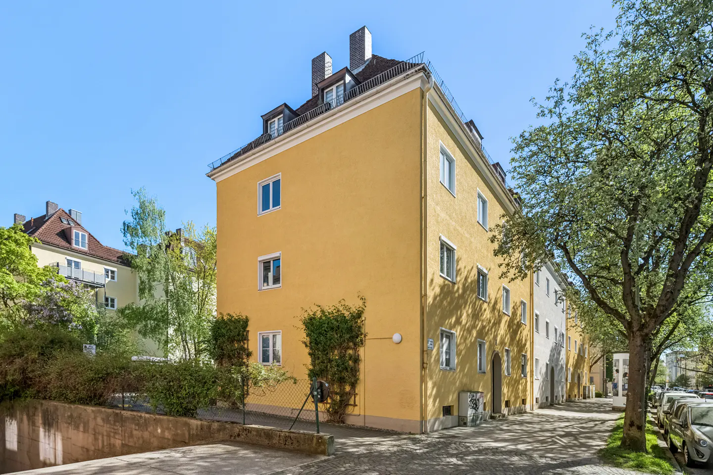A three-story yellow apartment building with white-framed windows and a dark roof on a sunny day.