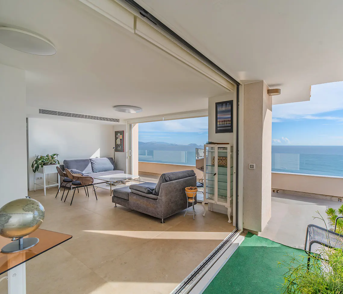 Bright, modern living room with gray sofas, chairs, and a globe. Large sliding doors open to a balcony with ocean views.