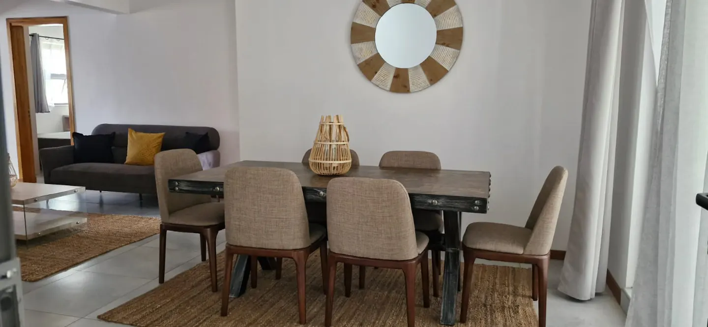 Living room with a dining table, six chairs, a sofa, and a round mirror on a white wall.