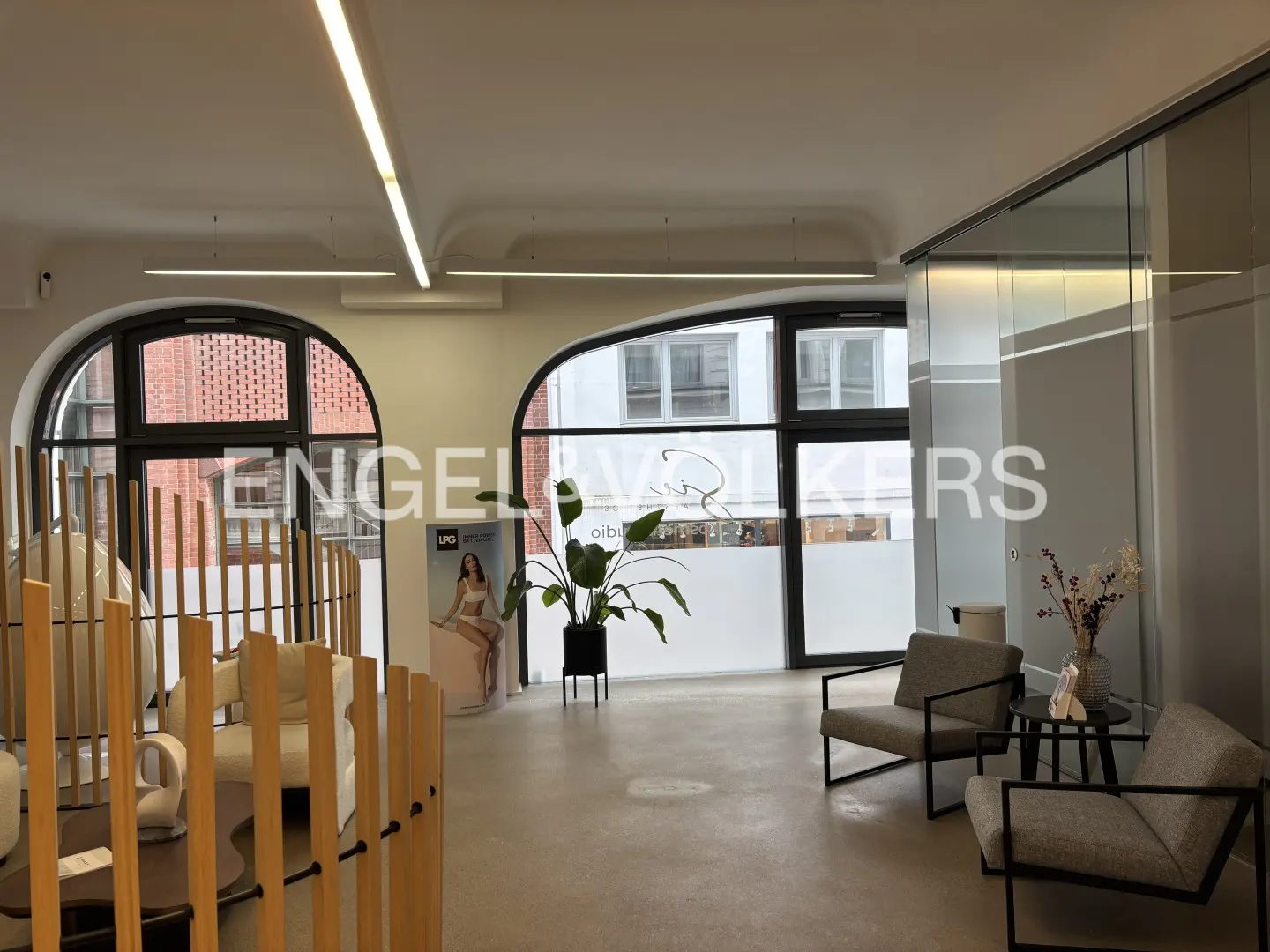Engel & Volkers office interior with arched windows, modern furniture, and a plant. The space is bright and airy.