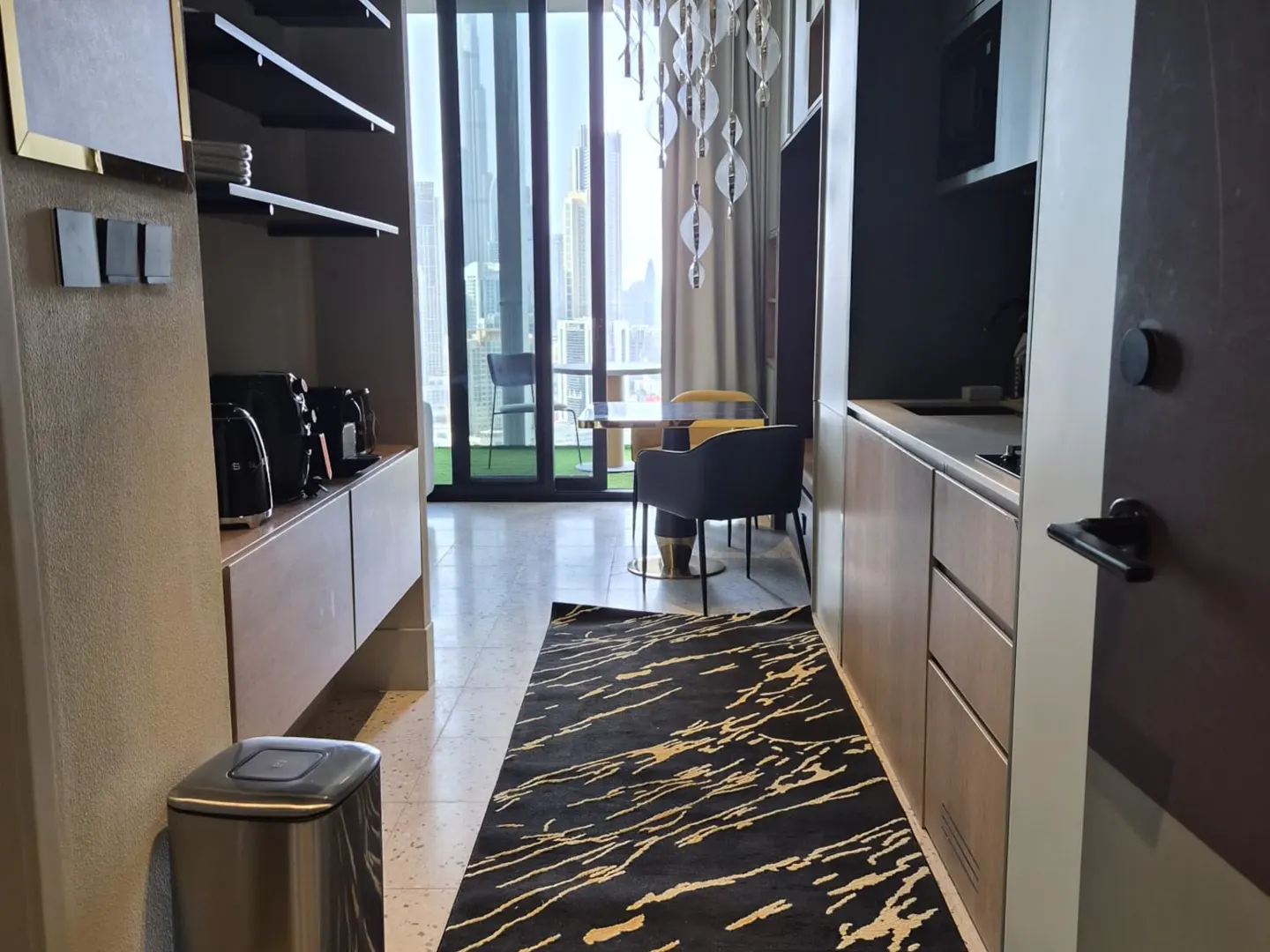 Modern kitchen with a black and gold rug, leading to a dining area with floor-to-ceiling windows and city skyline views.