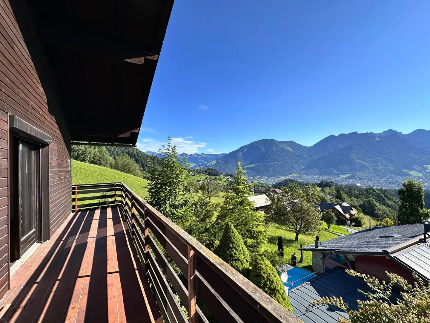 View from a wooden balcony with a mountain range in the background under a clear blue sky.