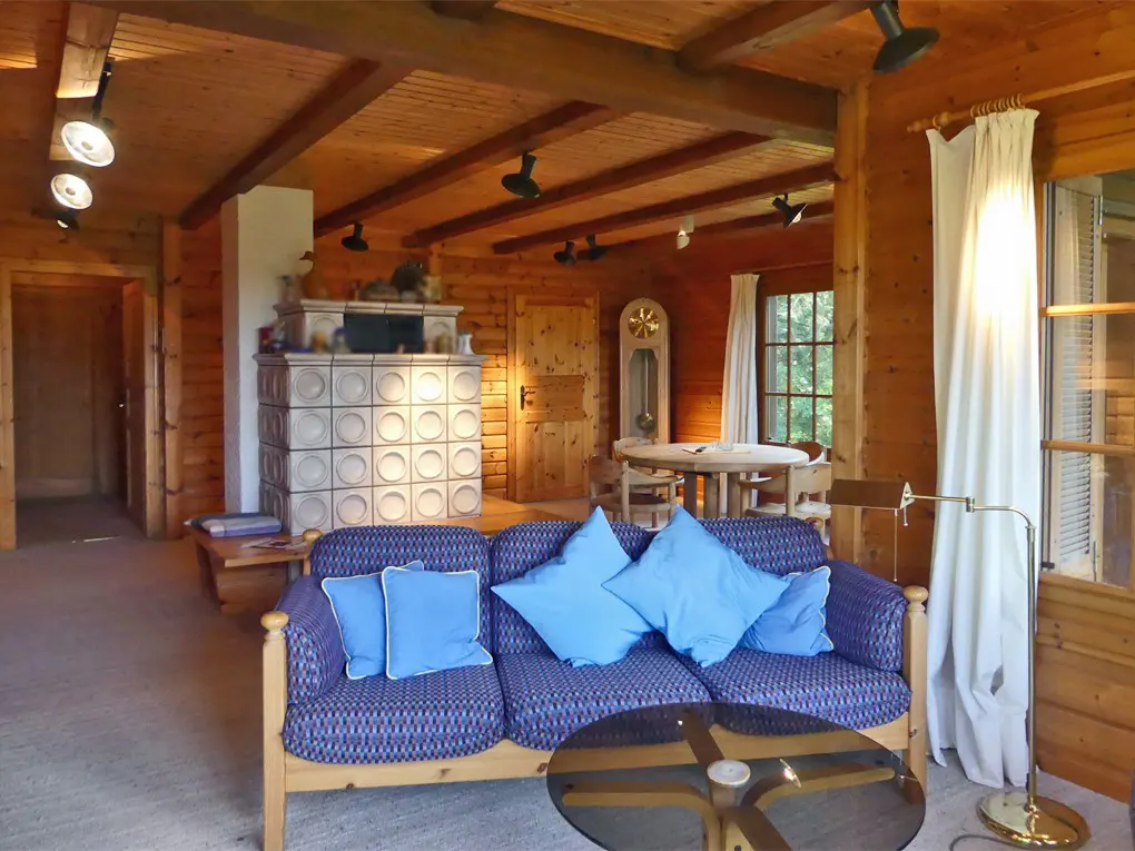 Living room with wood walls, blue sofa, and tiled fireplace. A round table and grandfather clock are in the background.