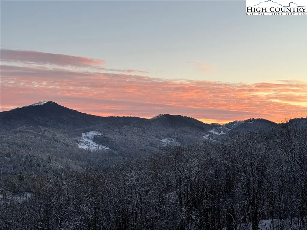 Snowy mountain landscape at sunset. Pink and orange clouds fill the sky above the snow-covered trees and hills.