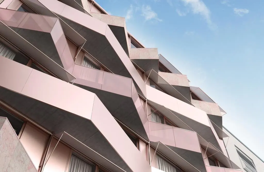Modern building with geometric balconies. The facade is pink and gray, with windows and curtains visible. Blue sky in the background.