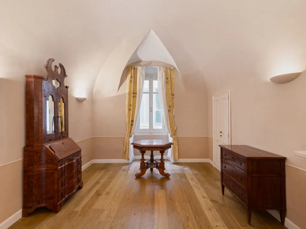 Attic room with wood floors, antique furniture, and a window with yellow curtains. Walls are two-toned, with sconces.
