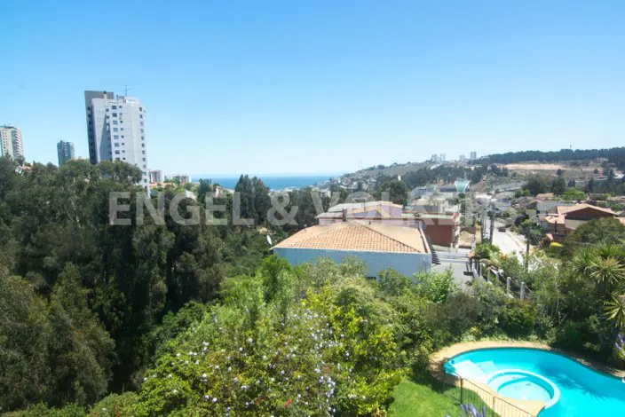 View of a city with a pool in the foreground, trees, buildings, and the ocean in the background under a blue sky.