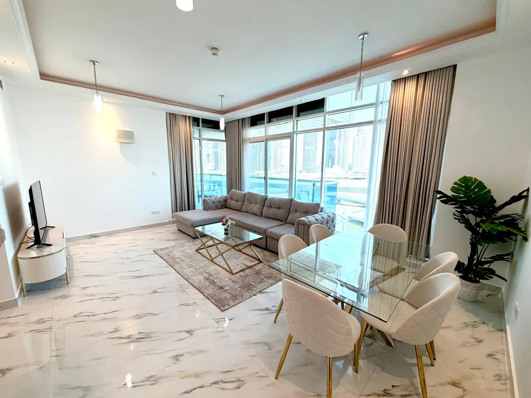 Modern open-plan living room with marble floors, a grey sectional sofa, glass coffee table, and dining set with city view.