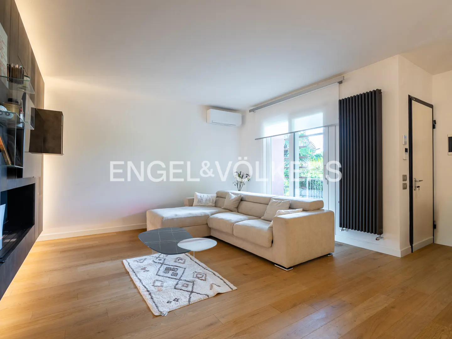 Living room with a beige sectional sofa, a patterned rug, and a black fireplace on a wooden floor.