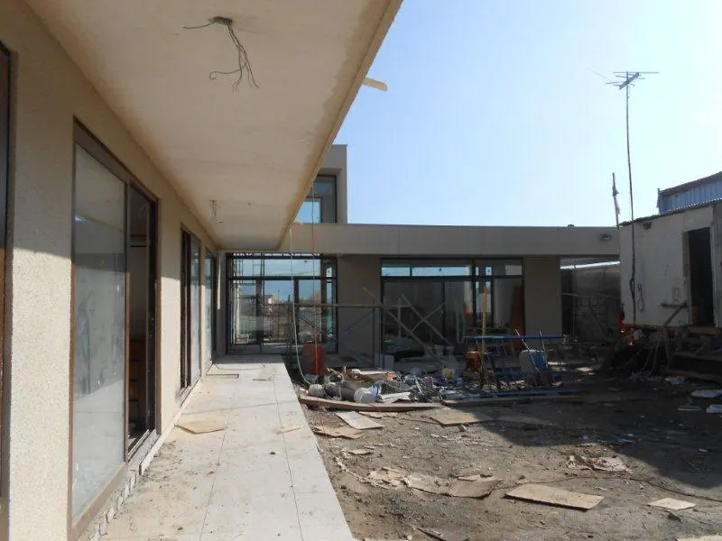 Exterior view of a building under construction with exposed wiring, large windows, and construction debris on the ground.