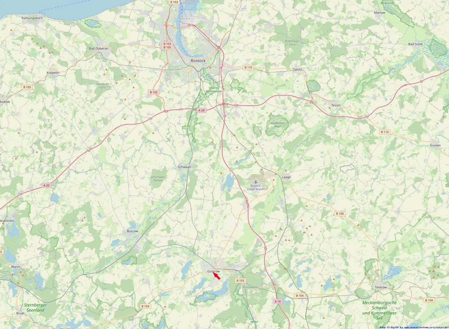 Map view of Güstrow, Germany, with an arrow pointing to the town. Roads and green spaces surround the area.