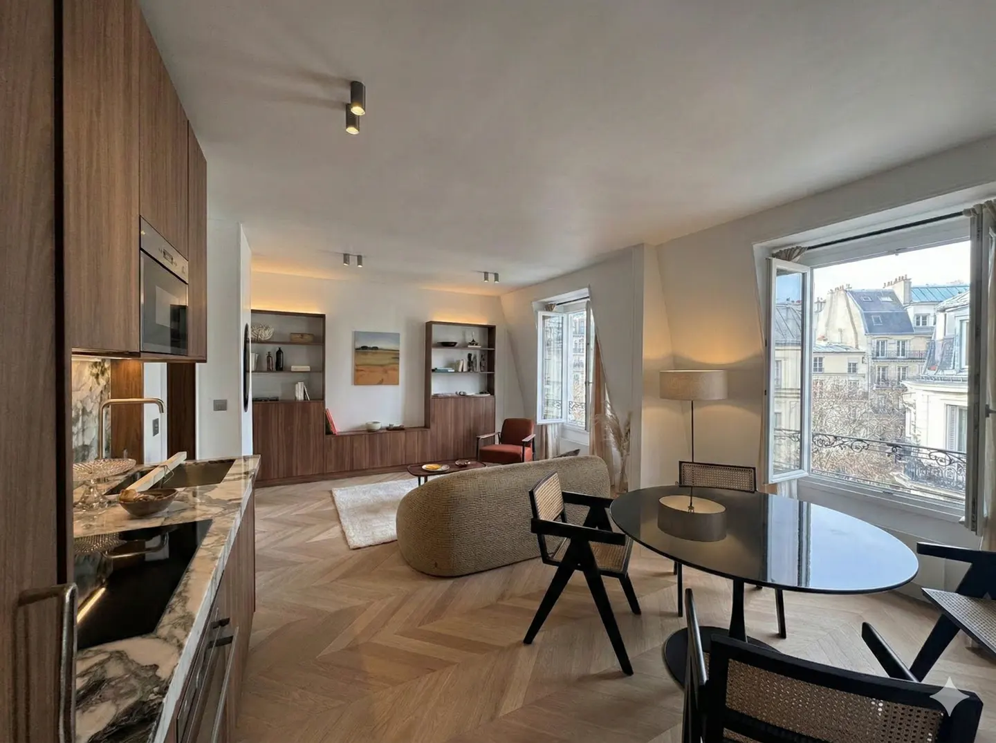Modern open-plan apartment with a marble kitchen, curved sofa, dining area, and large windows overlooking a city street.