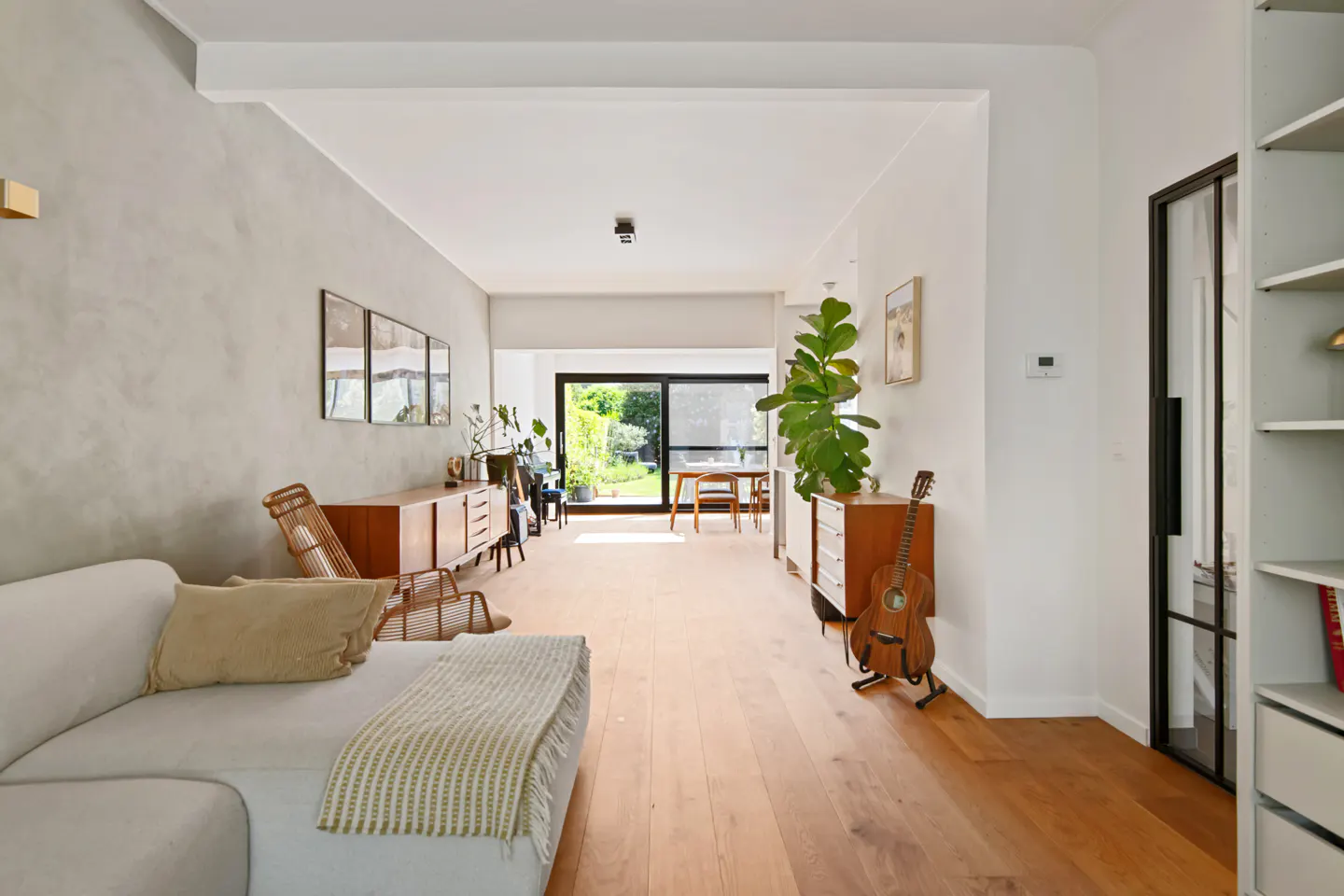 Modern living room with light wood floors, white sofa, mid-century furniture, a large fiddle leaf fig, and garden view.