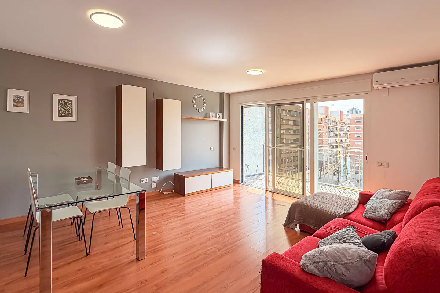 Bright living room with a red sofa, glass table, and sliding glass doors to a balcony with city views.