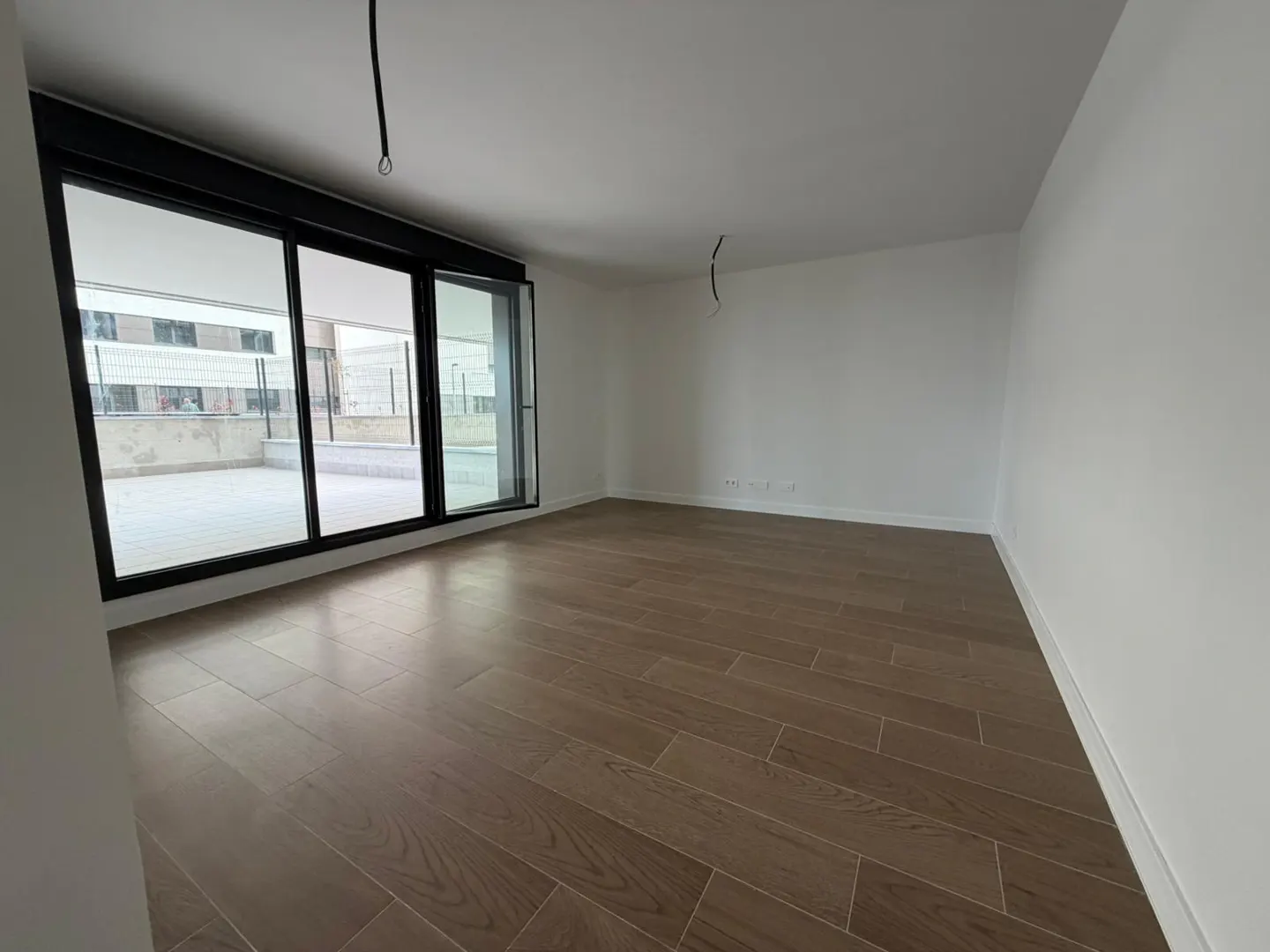 Empty room with brown wood floors, white walls, and a large black-framed sliding glass door to a balcony.